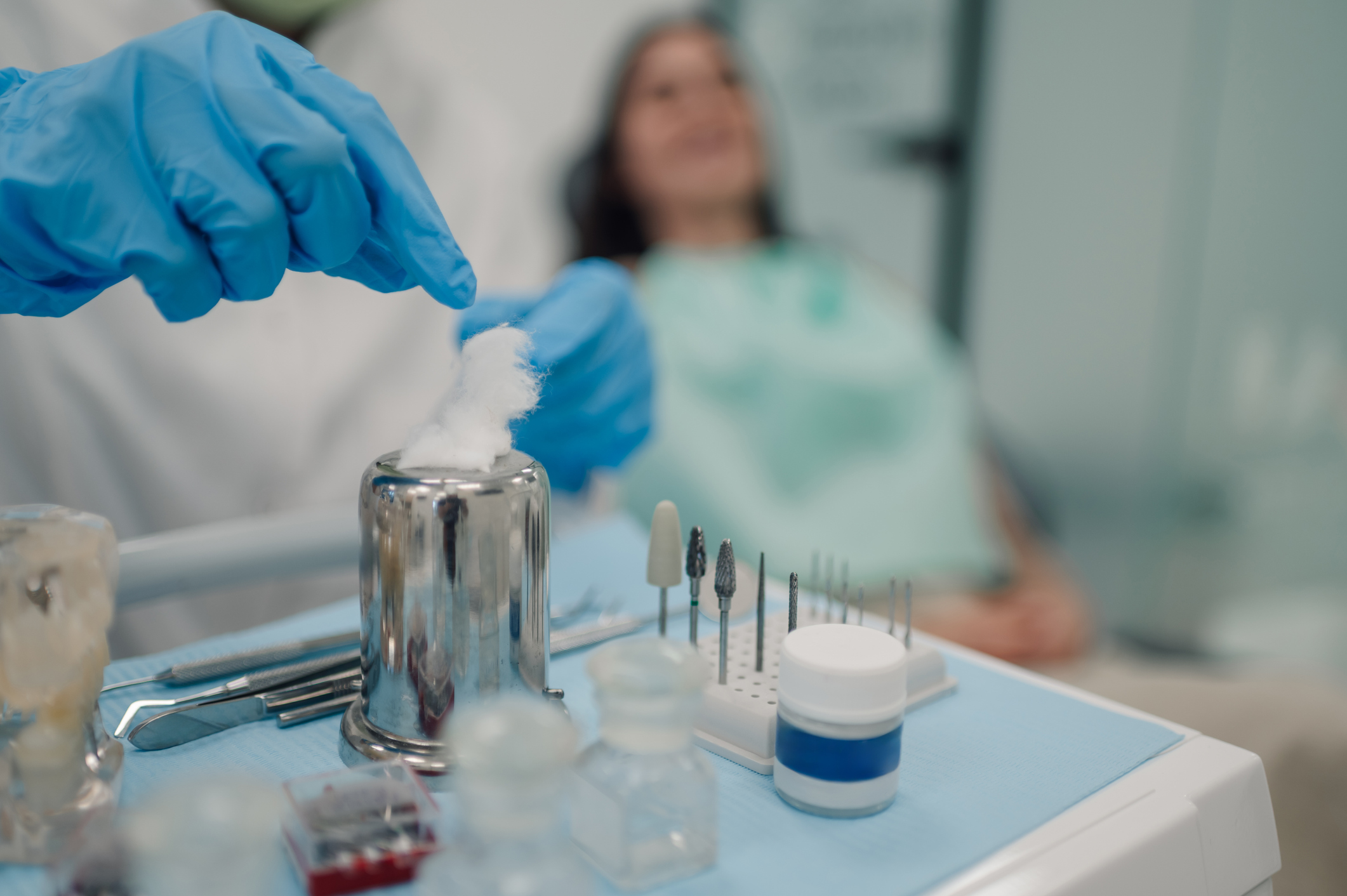 Dentist picking up cotton for dental procedure with patient in background